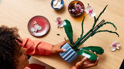 a top-down view of a woman assembling the lego orchid building kit at a wooden table