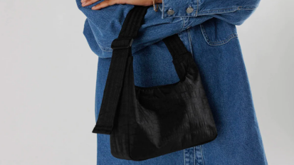 a close-up of a woman in an oversized denim shirt holding a black Baggu Mini Nylon Shoulder Bag