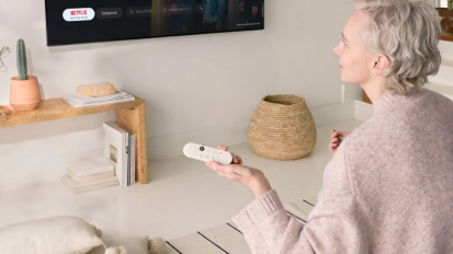 a woman in a pink sweater scrolling through netflix with a voice remote for chromecast in a beige living room