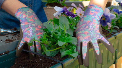 a close-up of a woman wearing patterned gardening gloves planting flowers