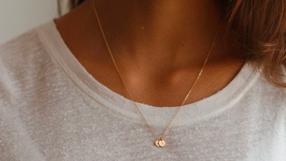 a close-up of a woman wearing a gold gldn initial necklace