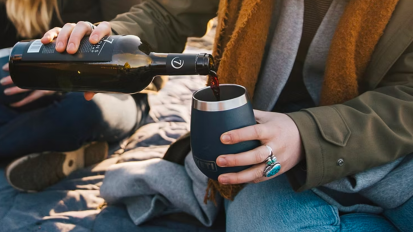 a close-up of a woman on a beach pouring red wine into a yeti rambler wine tumbler