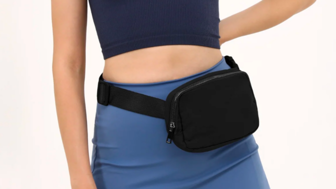 a close-up of a woman in a green crop top and a blue skirt wearing an ODODOS Mini Belt Bag around her hips
